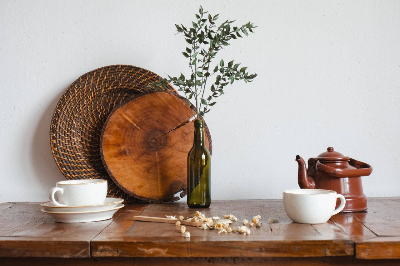 A cozy still life of tea cups, teapot, and rustic decor on a wooden table.