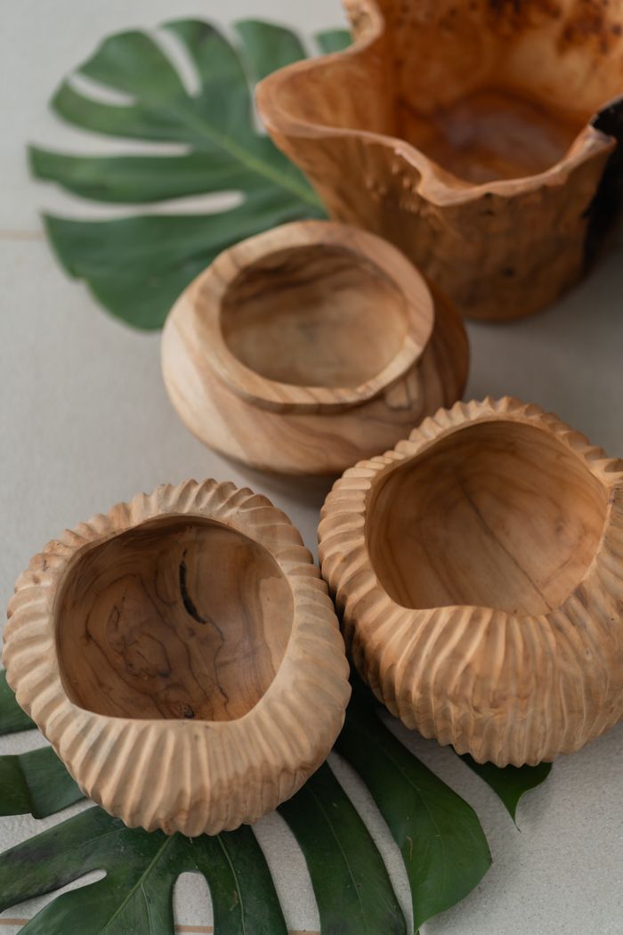 A collection of handcrafted wooden bowls displayed on monstera leaves, showcasing natural rustic decor.
