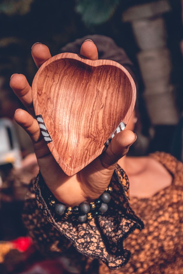 A heart-shaped wooden bowl held by an adult outdoors, showcasing craftsmanship.