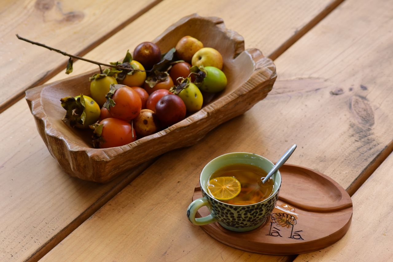 A cozy setup with a wooden bowl of fruits and a cup of herbal tea on a wooden table.