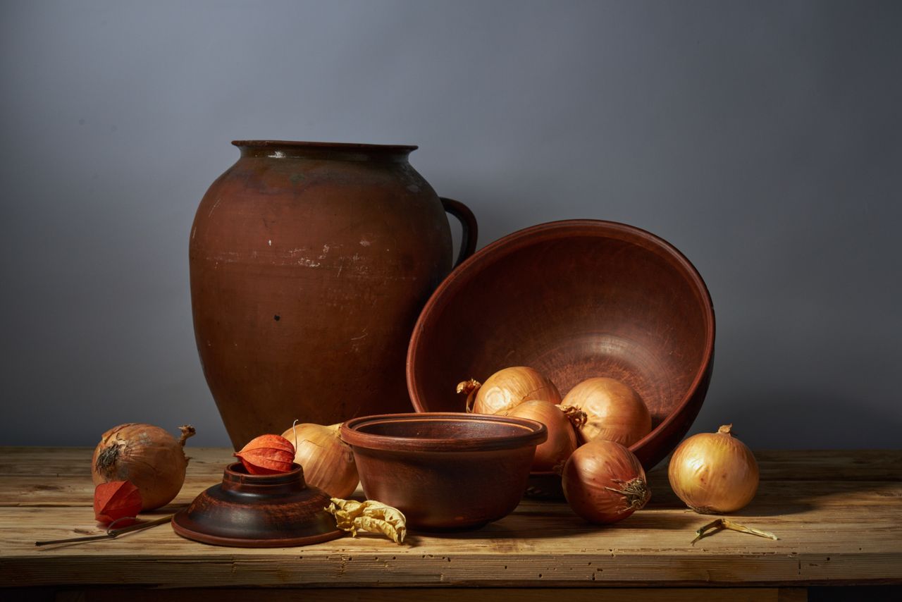 A rustic still life featuring clay pots and fresh onions on a wooden table.