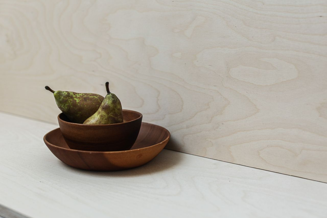 Close-up of green pears in wooden bowls on a light wooden surface.